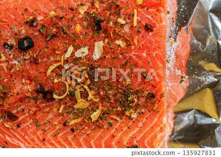 Macro close up of raw salmon fillet covered with dried herbs, spices, and garlic on crinkled aluminum foil Macro close up of raw salmon fillet covered with dried herbs, spices, and garlic on crinkled aluminum foil 135927831