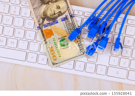 American 100 dollar bill on keyboard among Ethernet cables, linking finance digital technology. 135928041