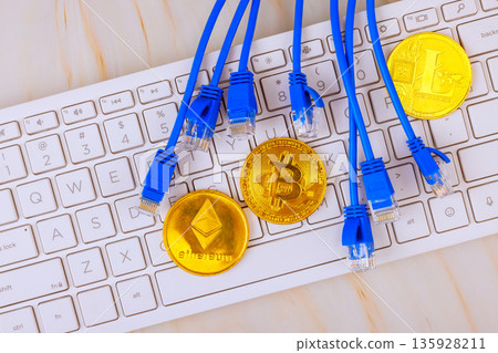 Various cryptocurrency coins are on keyboard with network cables connected to them in digital setting. 135928211