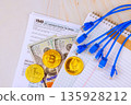 Tax return form lies with dollar cash cryptocurrency coins along with blue cables in accounting office setting. 135928212