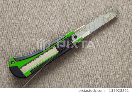 Close-up of isolated stationery retractable metallic knife with sharp blade on light cloth copy space background. Close-up of isolated stationery retractable metallic knife with sharp blade on light cloth copy space background. 135928231