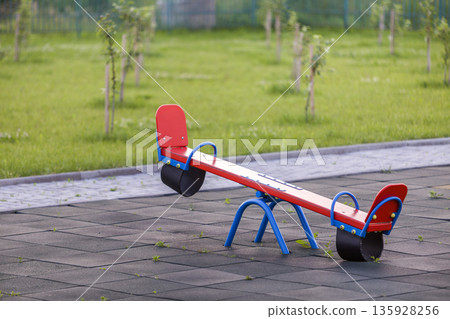 Seesaw swing in big yard with soft rubber flooring on sunny summer day. Seesaw swing in big yard with soft rubber flooring on sunny summer day. 135928256