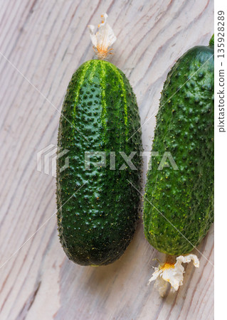 Vertical top view of two fresh cucumbers on a light wooden table with minimal background and copy space 135928289