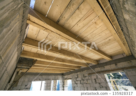 Close-up detail of house room interior under construction and renovation. Energy saving walls of hollow foam insulation blocks, wooden ceiling beams for roof frame. 135928317