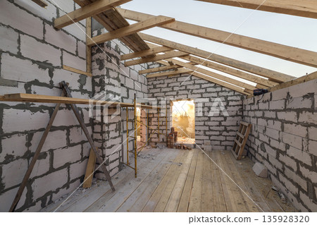 House interior under construction and renovation. Energy saving walls of hollow foam insulation blocks and bricks, ceiling beams and roof frame. House interior under construction and renovation. Energy saving walls of hollow foam insulation blocks and bricks, ceiling beams and roof frame. 135928320