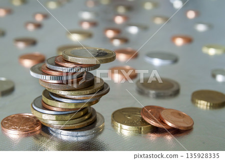 Pile of shiny coins different sizes and colors stacked unevenly on each other on colorful blurred blue abstract background. Money saving and financial risk concept. Pile of shiny coins different sizes and colors stacked unevenly on each other on colorful blurred blue abstract background. Money saving and financial risk concept. 135928335
