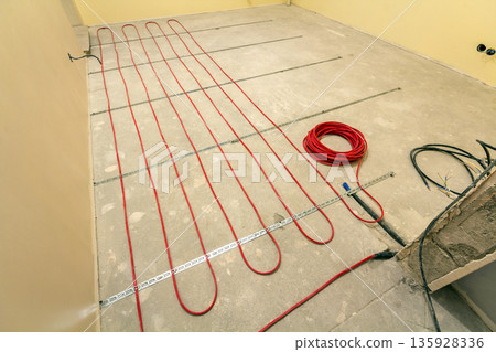 Heating red electrical cable wire roll on cement floor copy space background. Renovation and construction, comfortable warm home concept. Heating red electrical cable wire roll on cement floor copy space background. Renovation and construction, comfortable warm home concept. 135928336