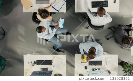 Top down view of corporate workers assessing business objectives and targets. Charts, diagrams and reports highlight progress and business intel for market research. Top down view of corporate workers assessing business objectives and targets. Charts, diagrams and reports highlight progress and business intel for market research. 135928361