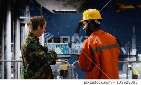 Security officer in camouflage uniform monitors offshore drilling operation, using radio communication for intelligence coordination and threat detection in maritime environments. Security officer in camouflage uniform monitors offshore drilling operation, using radio communication for intelligence coordination and threat detection in maritime environments. 135928385