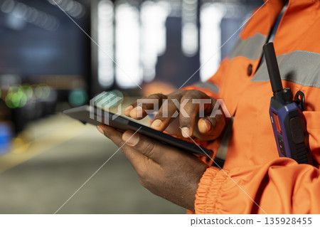 Close up of industrial worker in protective gear overseeing steel production with tablet, reflecting heavy labor and the automation development of the industrial factory as sparks rise. 135928455
