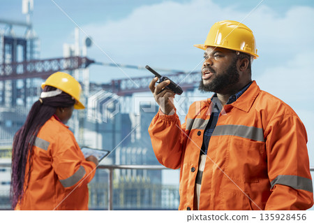 Petrol company manager on drilling barge using walkie talkie to ensure uninterrupted communication with employees. African american offshore platform worker transmits instructions through radio device 135928456