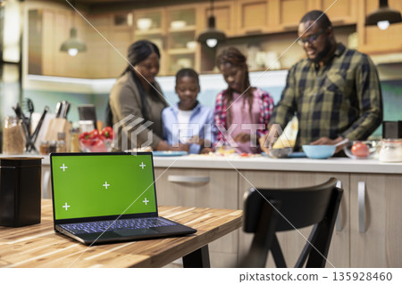 Chroma key on laptop next to black parents and kids making homemade pizza at the kitchen counter. Spreading sauce, layering mozzarella and sharing laughter. Cozy lifestyle full of joy. Chroma key on laptop next to black parents and kids making homemade pizza at the kitchen counter. Spreading sauce, layering mozzarella and sharing laughter. Cozy lifestyle full of joy. 135928460