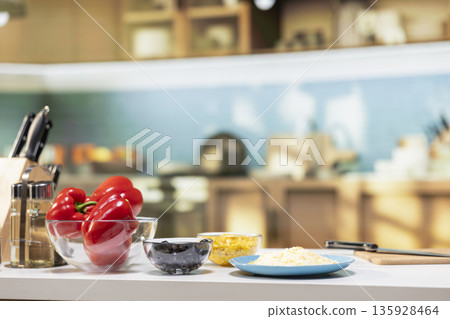 Empty kitchen island arranged with pizza essentials such as corn, mozzarella, red bell pepper and olives. Baking tools and utensils on countertop reflecting home cooking vibe on the weekend. 135928464
