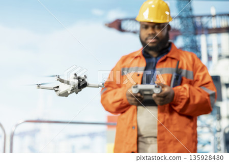 Close up of drone used by offshore platform professional doing site inspections. African american worker using aerial photography technology to determine optimal locations for drilling pads Close up of drone used by offshore platform professional doing site inspections. African american worker using aerial photography technology to determine optimal locations for drilling pads 135928480