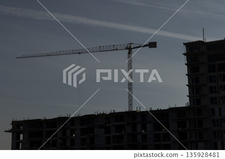 Metal crane standing tall over unfinished large concrete skyscraper building. Heavy machinery over steel construction framework showcasing new real estate architectural project Metal crane standing tall over unfinished large concrete skyscraper building. Heavy machinery over steel construction framework showcasing new real estate architectural project 135928481