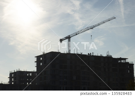 Construction workers working on roof of new real estate building being built during sunny day. Ironworkers cooperating to build new tall apartment complex, concept of growing city Construction workers working on roof of new real estate building being built during sunny day. Ironworkers cooperating to build new tall apartment complex, concept of growing city 135928483