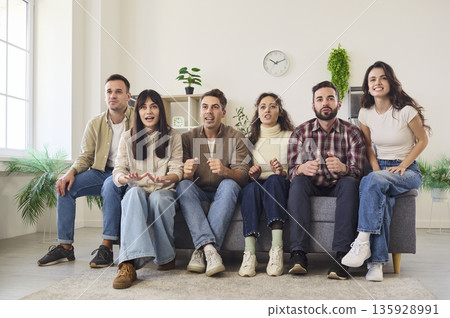 Friends on couch cheering as football fans watching TV together excited at home Friends on couch cheering as football fans watching TV together excited at home 135928991