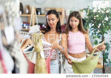 Near rack, mom with daughter buys tank top, chooses items. Near rack, mom with daughter buys tank top, chooses items. 135929384