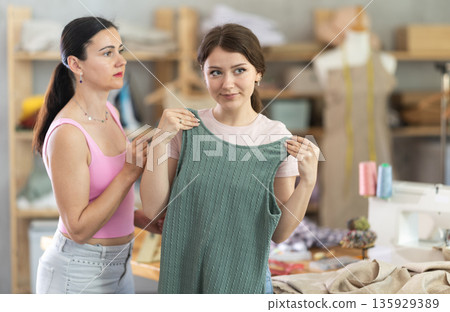 Girl customer examines finished product in presence of female tailor Girl customer examines finished product in presence of female tailor 135929389
