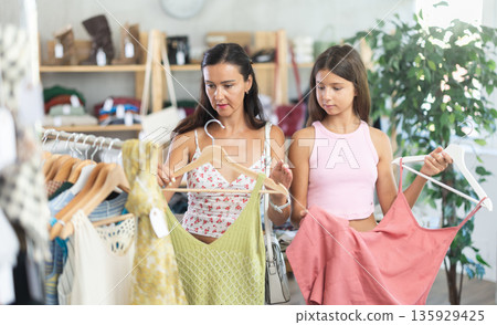 Near rack, mom with daughter buys summer dress, chooses items. Near rack, mom with daughter buys summer dress, chooses items. 135929425