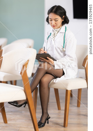 Young woman in medical coat taking notes on tablet in lecture hall Young woman in medical coat taking notes on tablet in lecture hall 135929465