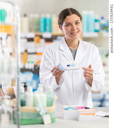 Female pharmacist offering ointment near the counter Female pharmacist offering ointment near the counter 135929481