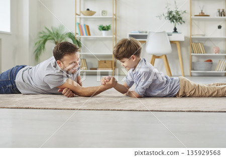 Happy dad and little son are lying on the floor and having an arm wrestling contest 135929568