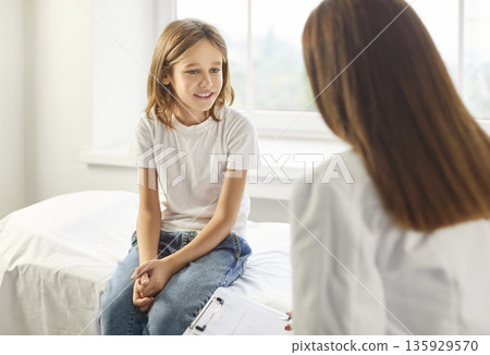 Female doctor talking with a child boy patient during medical examination in clinic. 135929570