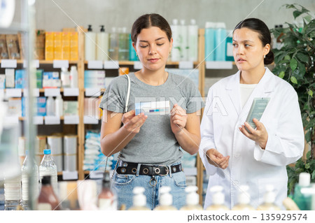 Young woman choosing ointment while pharmacist offering in drugstore Young woman choosing ointment while pharmacist offering in drugstore 135929574