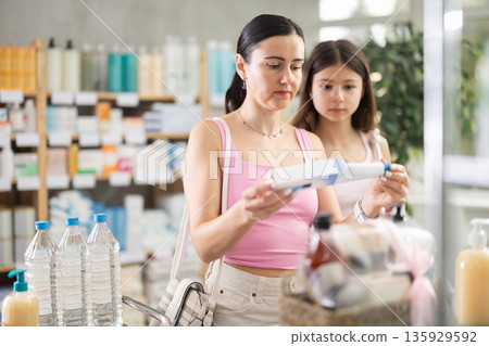 Mom and daughter customer choosing ointment in box in drugstore Mom and daughter customer choosing ointment in box in drugstore 135929592
