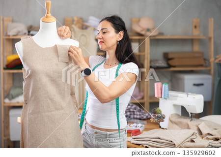 Woman tailor connects parts of dress on mannequin 135929602