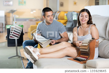 In exhibition hall,couple sat down on gray sofa and keep sets of upholstery material samples 135929645