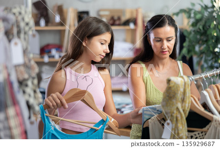 Mother and teenage daughter choosing something for summer in clothing store Mother and teenage daughter choosing something for summer in clothing store 135929687