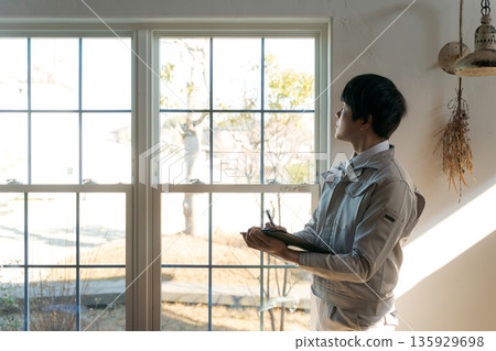 A man in work clothes looking at a window indoors 135929698