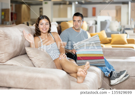 Cheerful couple choosing upholstery for lounge furniture in store Cheerful couple choosing upholstery for lounge furniture in store 135929699