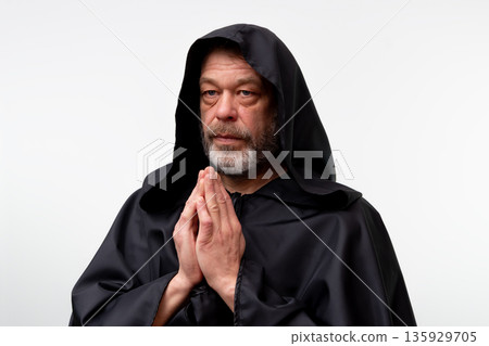 Old male monk praying while standing isolated on white studio background. Old male monk praying while standing isolated on white studio background. 135929705