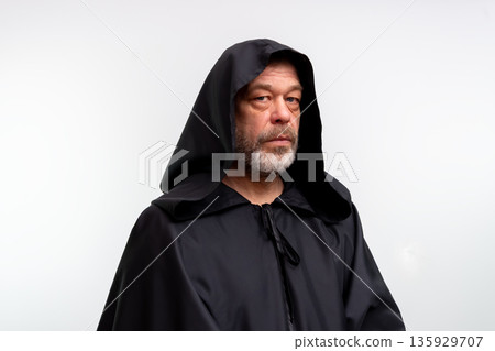 Old male monk in dark monastic clothing isolated in studio on white background. Old male monk in dark monastic clothing isolated in studio on white background. 135929707