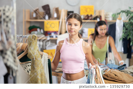 Happy teenage girl choosing something for summer in clothing store Happy teenage girl choosing something for summer in clothing store 135929730