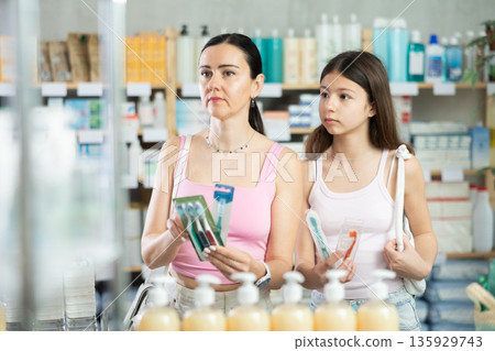 Woman buyer with teen daughter select toothbrush in drug store Woman buyer with teen daughter select toothbrush in drug store 135929743