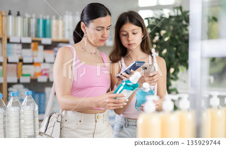 Woman with teen daughter in pharmacy scans QR code on mouthwash Woman with teen daughter in pharmacy scans QR code on mouthwash 135929744