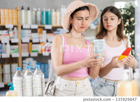 Woman buyer with teen daughter select sunblock cream in drug store 135929847