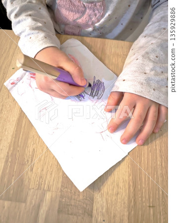 A child draws on white paper with a wax crayon, viewed from above. A child draws on white paper with a wax crayon, viewed from above. 135929886