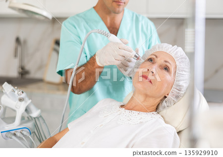 Male dermatologist performing cosmetology procedure for elderly woman, RF lifting and deep hydration for facial skin therapy Male dermatologist performing cosmetology procedure for elderly woman, RF lifting and deep hydration for facial skin therapy 135929910