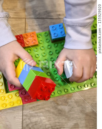 A small child builds a house from bright construction blocks on a green platform. 135929920