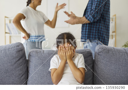 Distressed child covering face as parents argue at home, family conflict theme Distressed child covering face as parents argue at home, family conflict theme 135930290