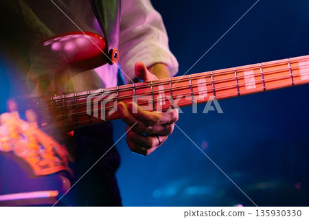 Close-up of hand playing red electric bass guitar under stage lights Close-up of hand playing red electric bass guitar under stage lights 135930330