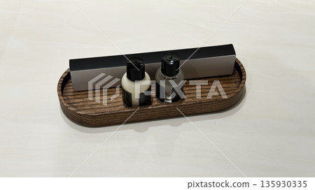 Two small bottles with black caps and a rectangular box placed on an oval wooden tray on a white surface. Two small bottles with black caps and a rectangular box placed on an oval wooden tray on a white surface. 135930335