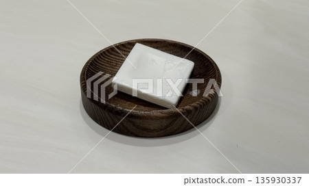 White bar soap on wooden soap dish on white surface, close-up White bar soap on wooden soap dish on white surface, close-up 135930337