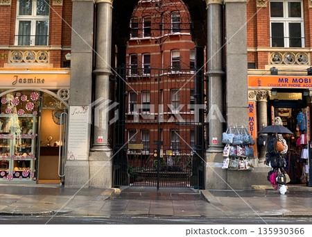 LONDON, UK, October 22, 2019, ondon street facade with brick building, stone columns, wrought iron gate, and shop signs Jasmine and MR MOBI, wet pavement LONDON, UK, October 22, 2019, ondon street facade with brick building, stone columns, wrought iron gate, and shop signs Jasmine and MR MOBI, wet pavement 135930366