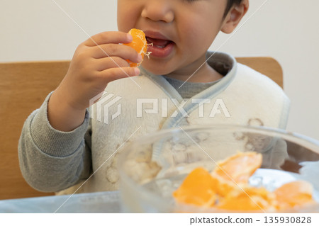 A boy eating a mandarin orange with his hands 135930828